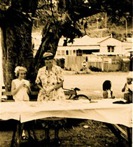 Mrs Radford, also know as Granny Radford, setting up tables under the coral tree in the square at Wagstaffe, in preparation for a stall or a party.